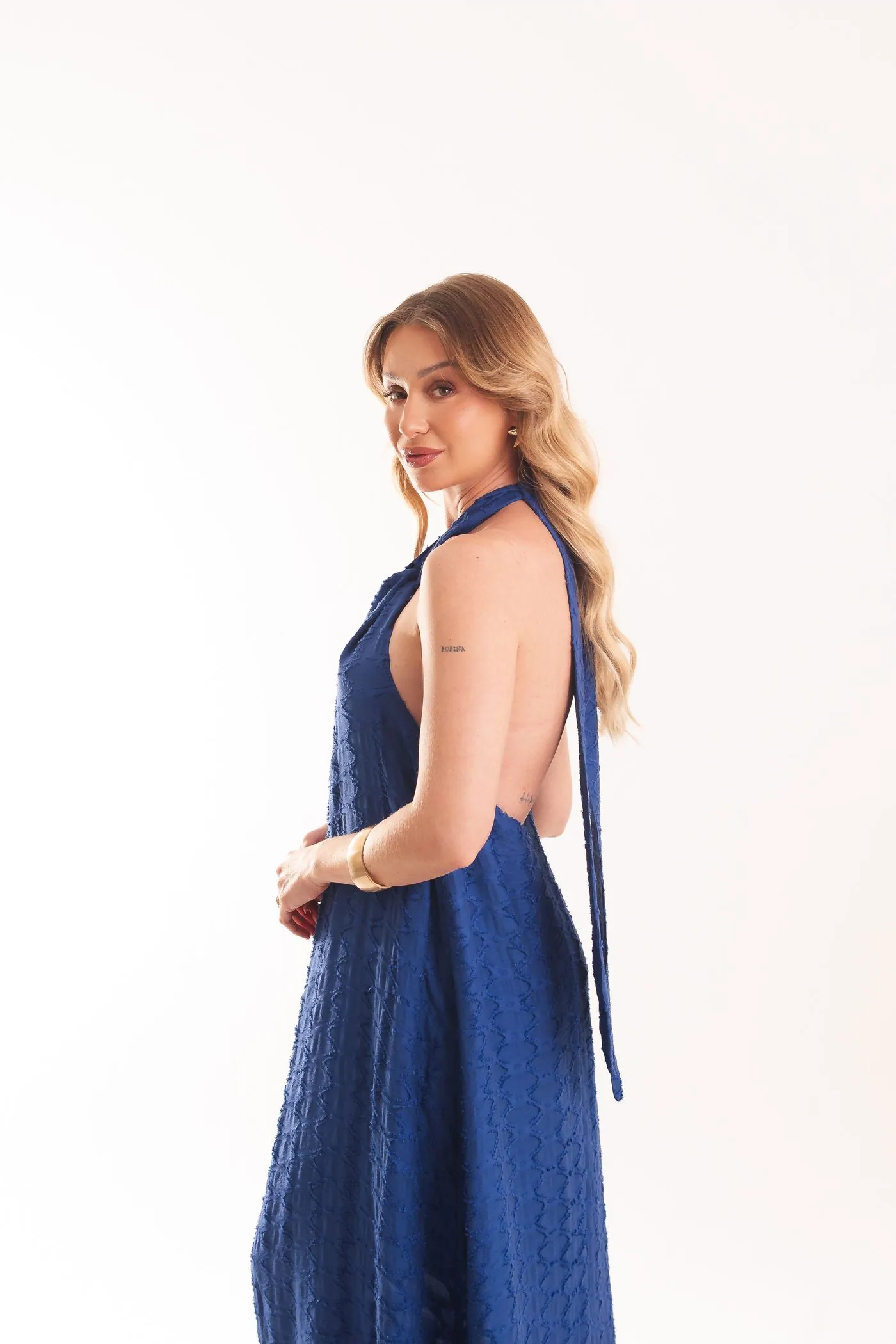 Vestido Búzio visto de lado, com o nó no pescoço, as costas abertas e a saia longa azul